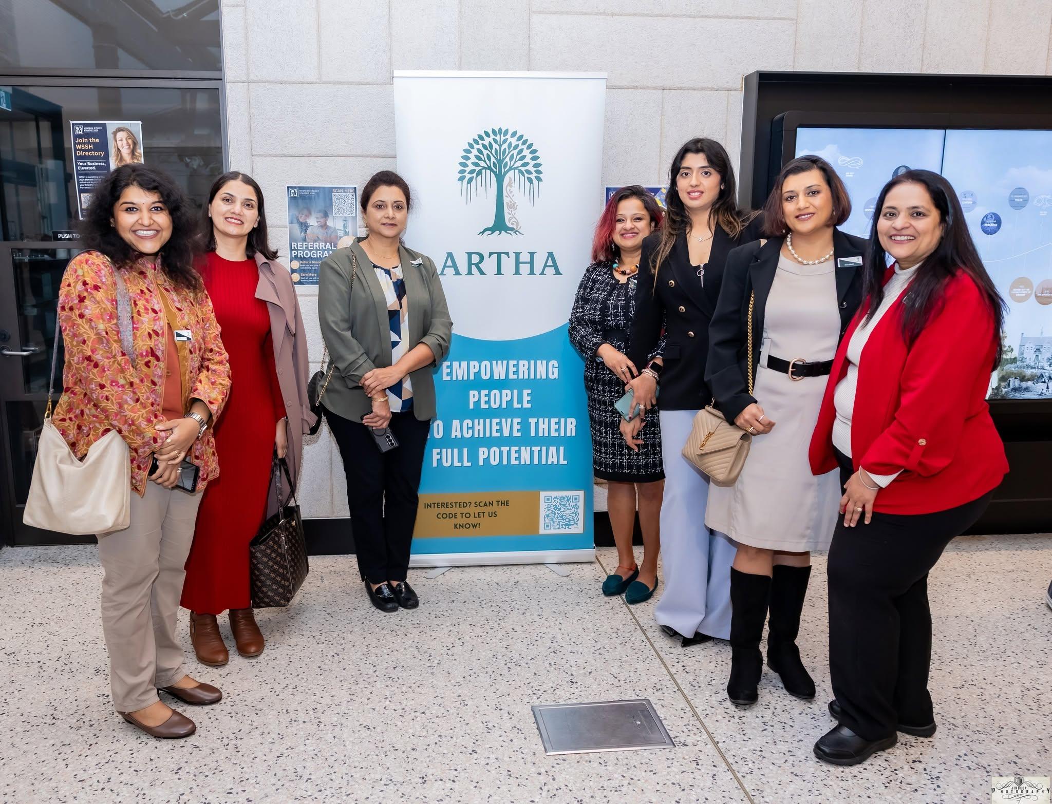 Seven members standing together beside the Artha banner at a community evening.