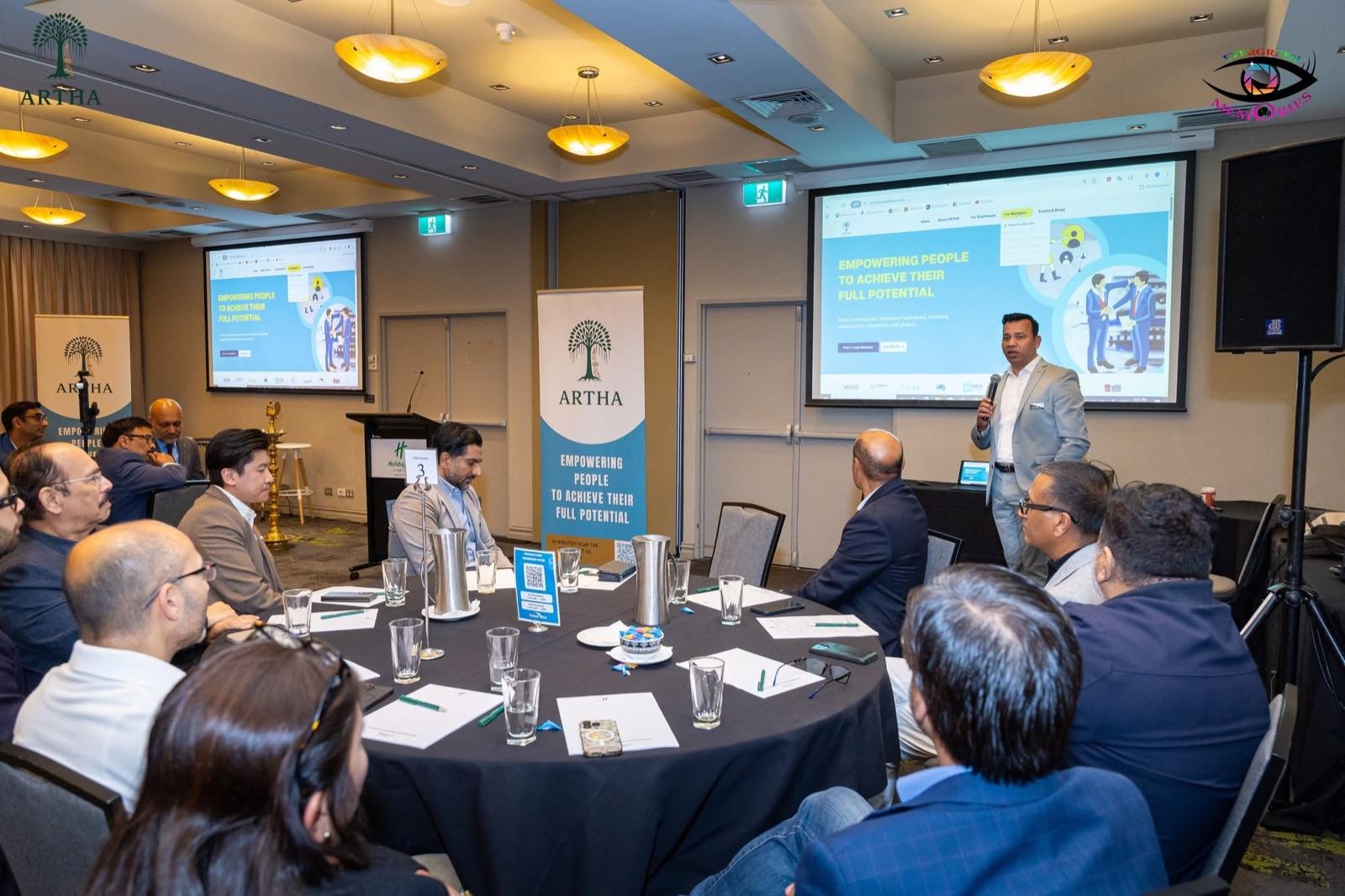 Guests around a table as a speaker presents at the Artha Soft Launch Event.